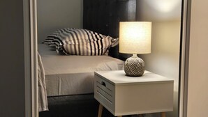A bedroom with a bed, a bedside table with a lamp, and a mirror. - Cozy Family-sized basement suite. (Winnipeg)