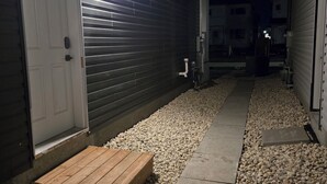A nighttime view of a residential area with a wooden deck, a gravel pathway, and a white door. - Cozy Family-sized basement suite. (Winnipeg)