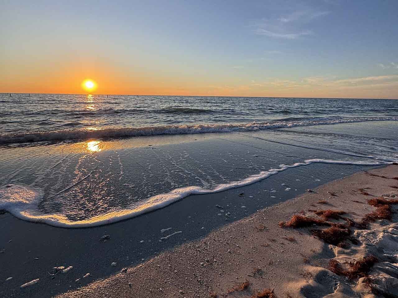 Ein Strand bei Sonnenuntergang, wobei die Sonne sich im Wasser und Sand spiegelt.