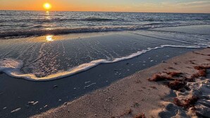 A beach at sunset with the sun reflecting on the water and sand.