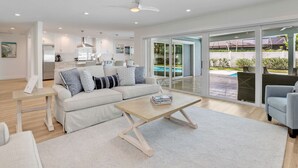 A modern living room with a white sofa, a coffee table, and a view of a swimming pool through large glass doors.
