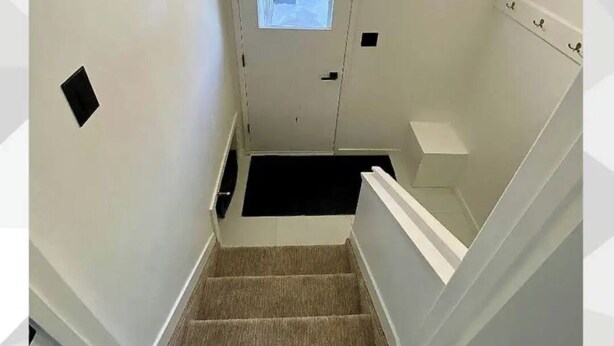 Un escalier dont les marches sont recouvertes de moquette, menant à une porte dotée d’une petite fenêtre.