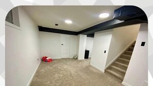 Un sous-sol spacieux avec un revêtement de sol beige, un escalier et une porte donnant sur une autre pièce.