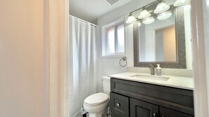 Un baño con inodoro blanco, tocador oscuro y espejo con luces.
