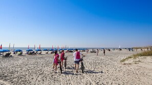 Een zandstrand met mensen, fietsen en kleurrijke parasols.
