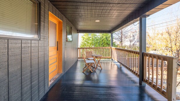 Un portico coperto con ringhiera in legno, un tavolo e sedie, e una porta che dà su un ambiente interno.
