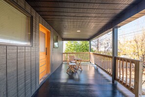 A covered porch with a wooden railing, a table and chairs, and a door leading to an interior space.