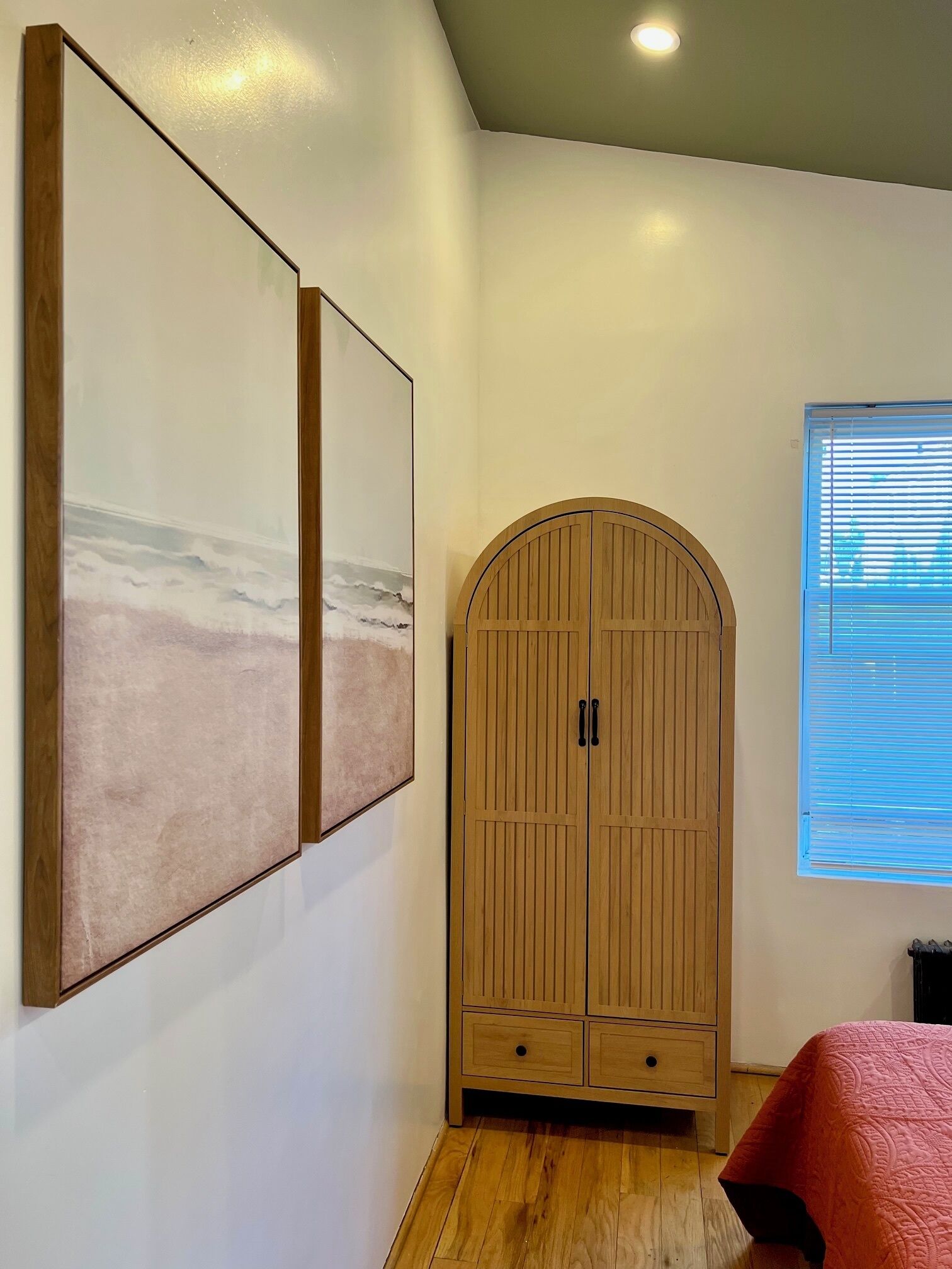 Une pièce avec une armoire en bois, une fenêtre avec des stores et deux grandes peintures abstraites accrochées au mur.