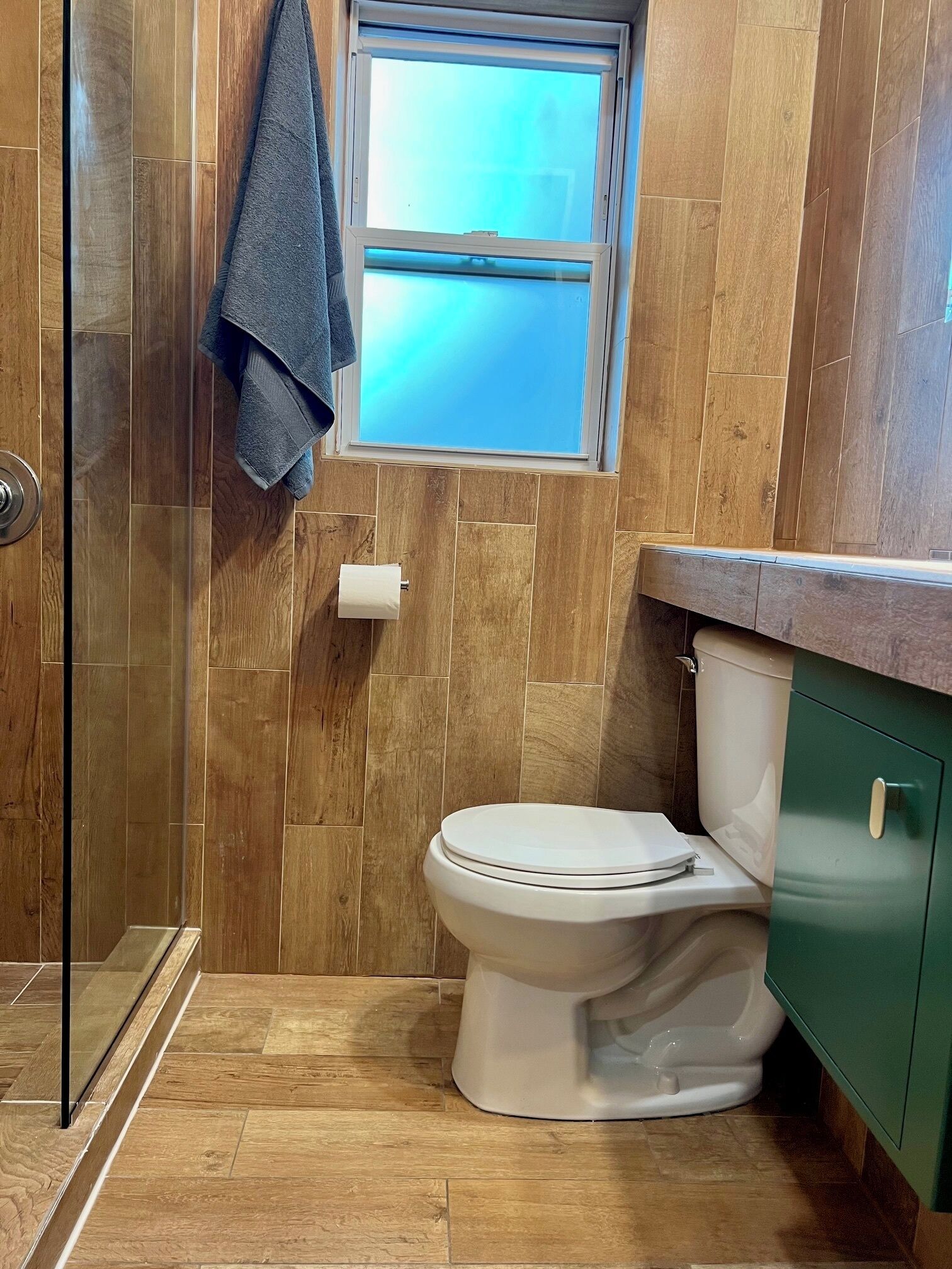 A bathroom with wooden panel walls, a toilet, a window, and a towel hanging on a rack.