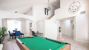 A spacious living area with a pool table, a dining area with blue chairs, and a staircase leading to an upper level. - Chic Vegas House w/Game Room + BBQ (North Las Vegas)