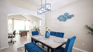 A dining area with a marble table, blue upholstered chairs, and a blue vase with flowers. - Chic Vegas House w/Game Room + BBQ (North Las Vegas)