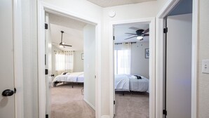 A hallway leading to two bedrooms with carpeted floors and white walls. - Chic Vegas House w/Game Room + BBQ (North Las Vegas)