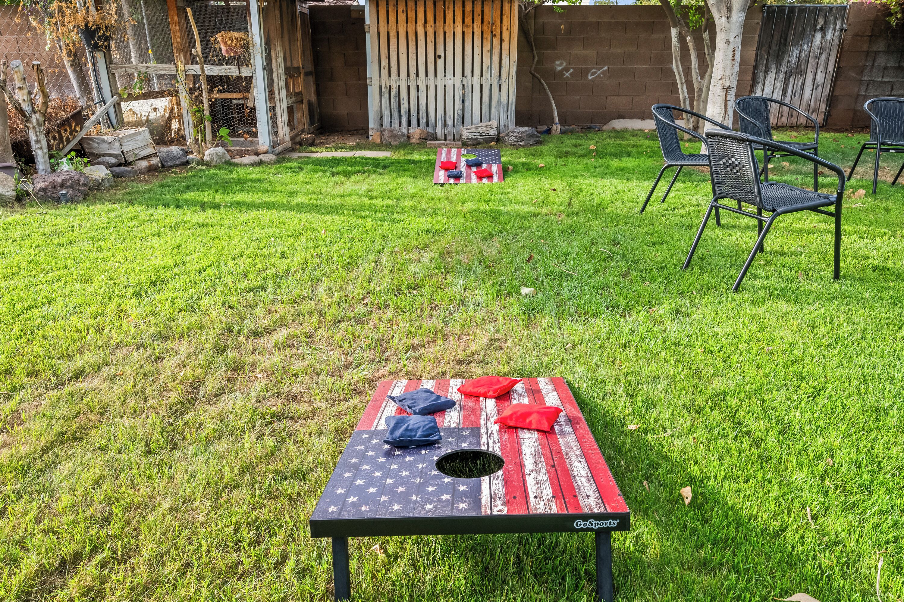 A backyard with a picnic table featuring a red, white, and blue design, surrounded by chairs and a small play area.