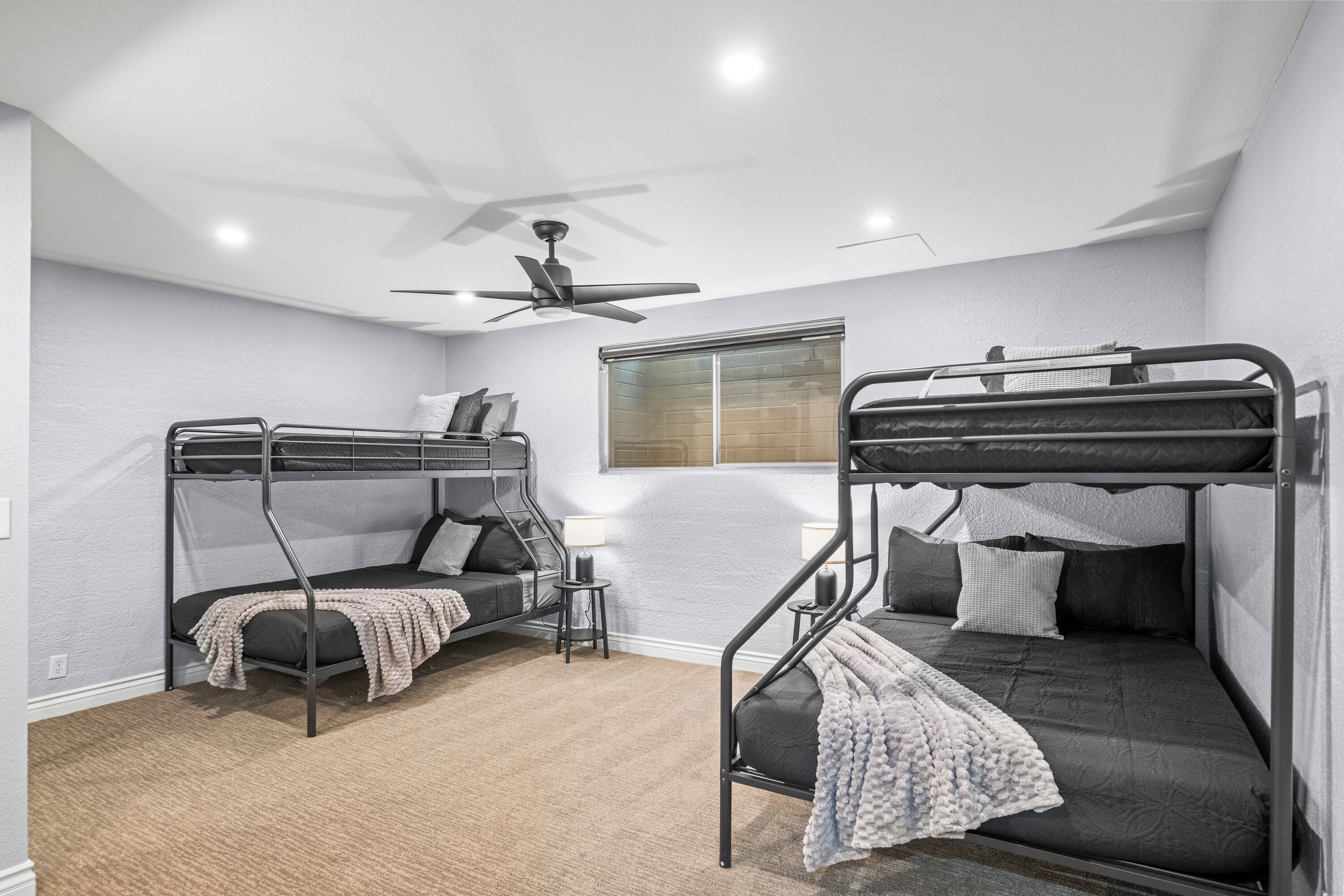 A bunk bed room with a ceiling fan, a window, and a small table.