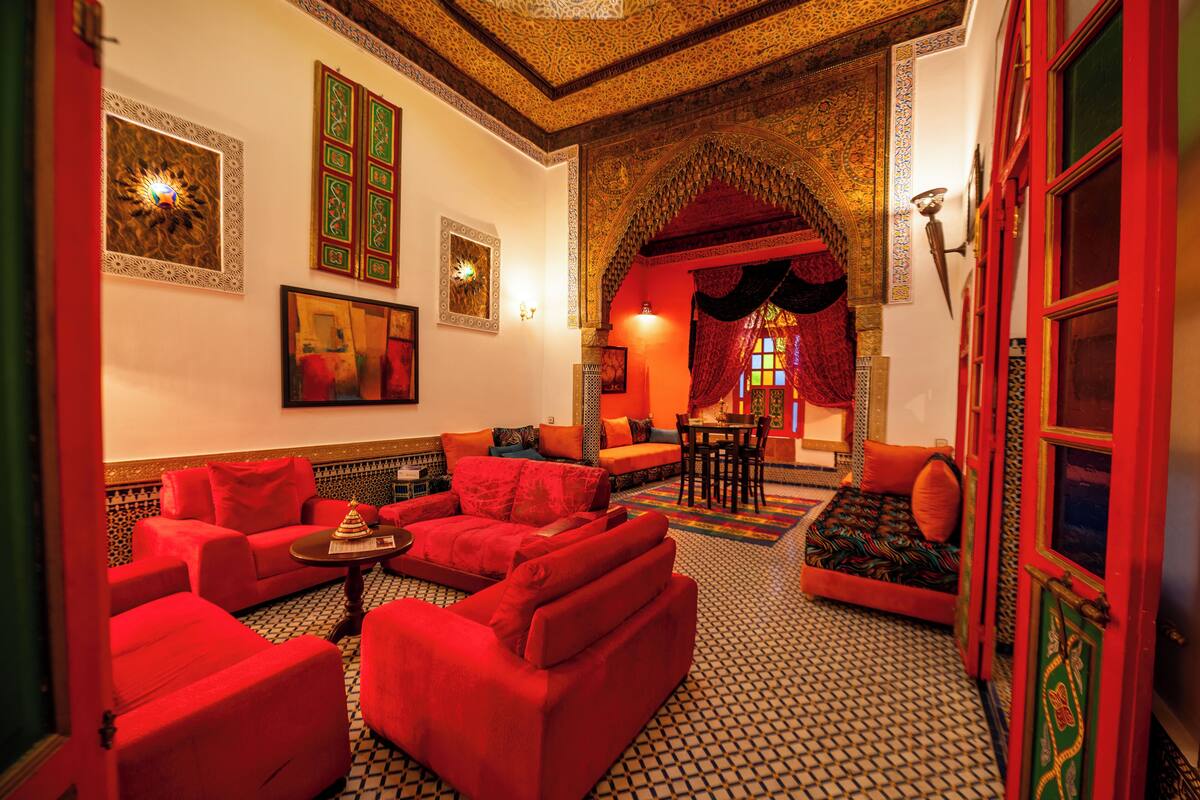A traditional Moroccan interior with red sofas, patterned floor tiles, and ornate wall decorations.