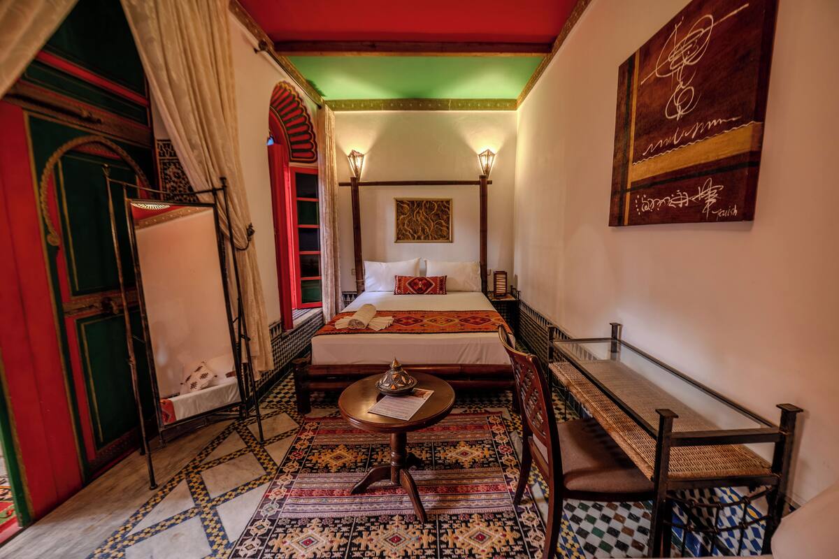 A traditional room with a four-poster bed, a small round table, and a bench.