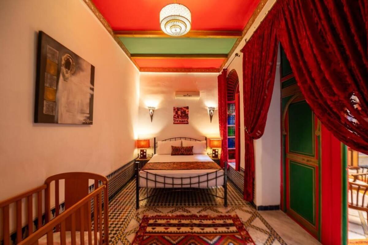 A room with a bed, a wooden chair, a chandelier, and a red curtain.