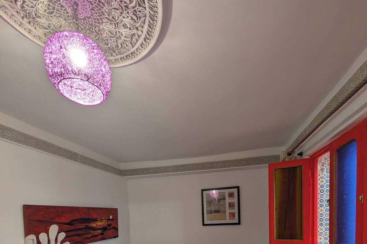 A neatly arranged bedroom with a patterned bedspread, a decorative ceiling light, and a framed picture on the wall.
