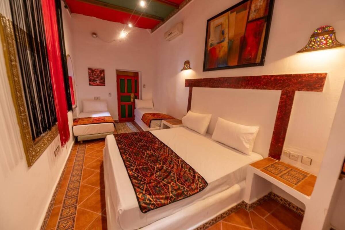 A hotel room with a bed, a small sofa, a nightstand, and a red door.