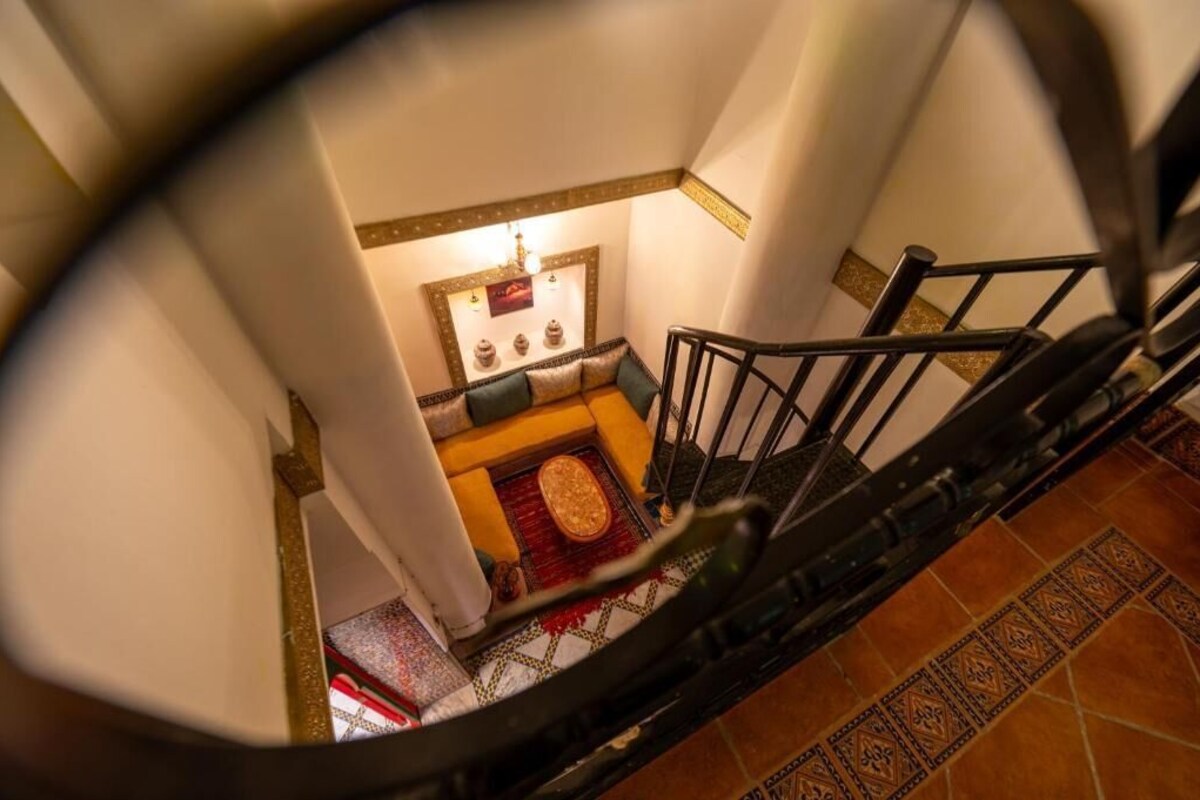 A spiral staircase with a view of a room below, featuring a patterned floor, a small rug, and a decorative wall piece.