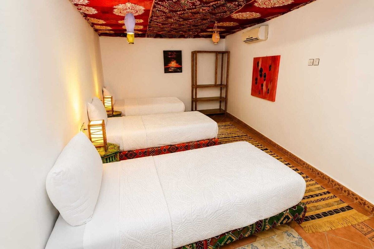 A narrow hallway with two white beds, patterned rugs, and a decorative ceiling.