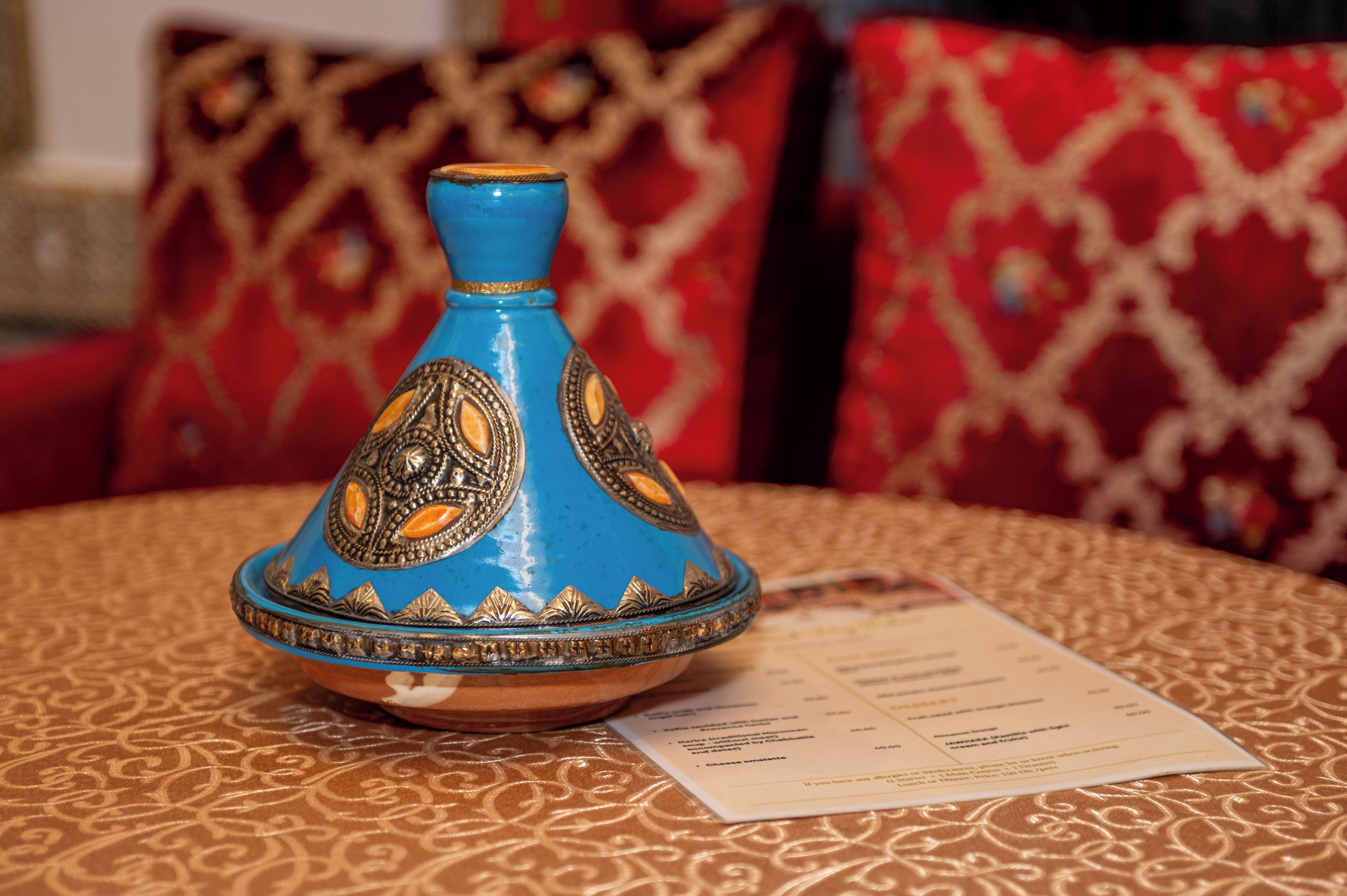 A blue and orange decorative item on a patterned tablecloth with a menu.