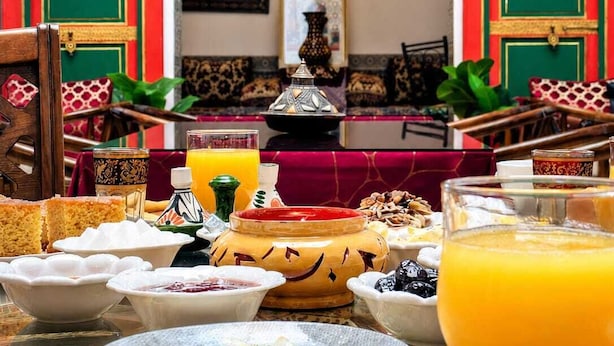 En frukostuppdukning med ett bord för två personer, inklusive tallrikar med mat, ett glas apelsinjuice och en traditionell marockansk tagine.