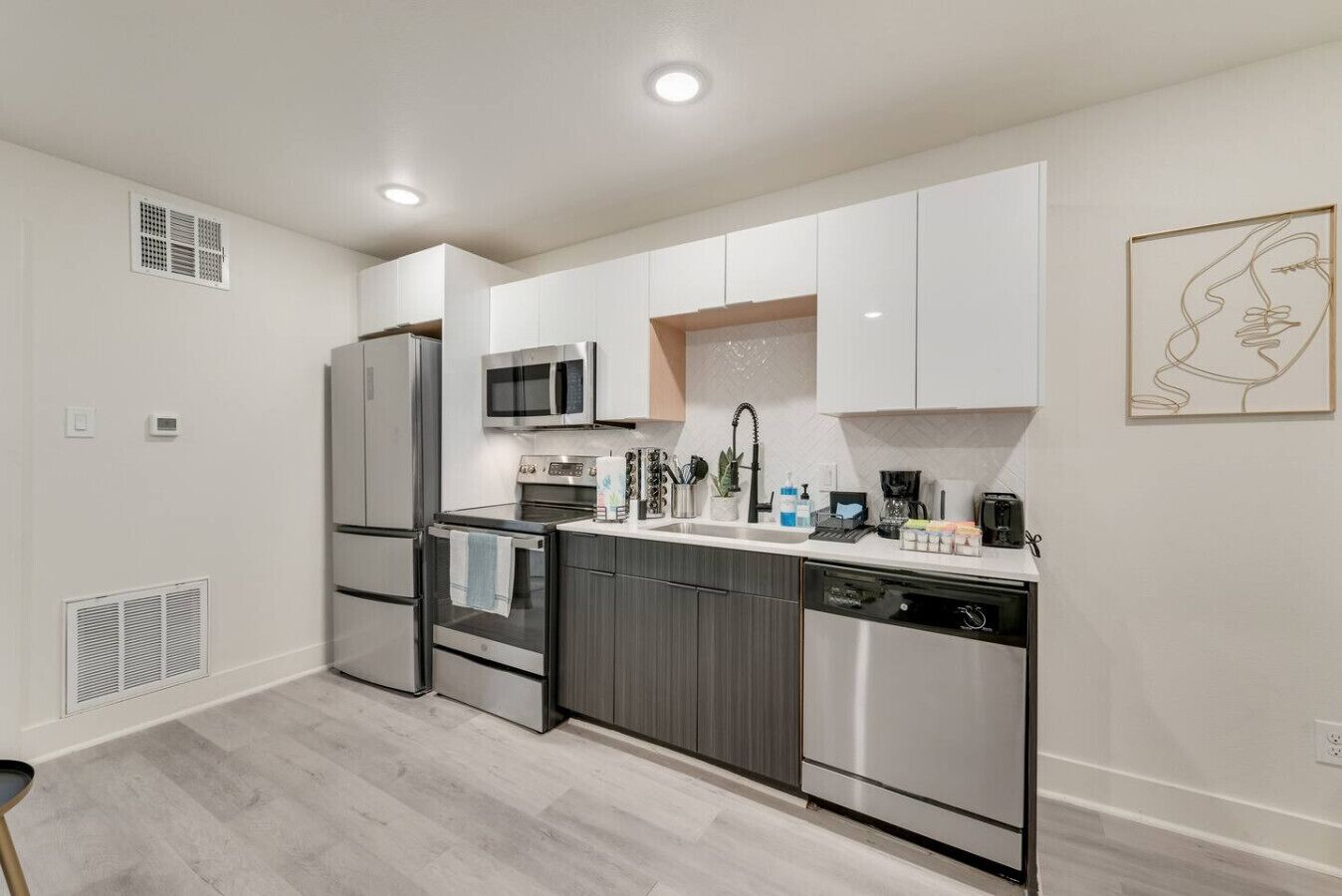 Una cocina moderna con armarios blancos y grises, electrodomésticos de acero inoxidable y un diseño limpio y minimalista.