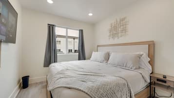 Un dormitorio con cama, mesita de noche, ventana con cortinas y una obra de arte en la pared.