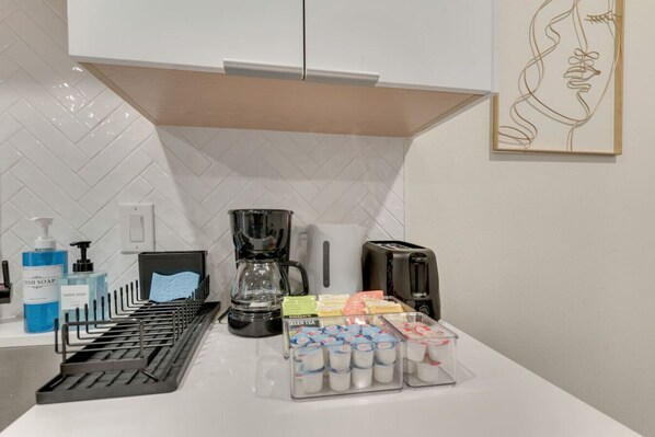 Une cuisine équipée d’une machine à café, d’un grille-pain et de récipients contenant du thé et du lait.