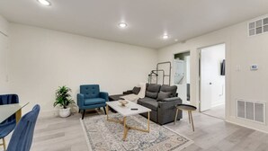 A modern living room with a sofa, armchair, coffee table, and a dining area with chairs and a table. - Stylish City Getaway | Near Deep Ellum & Downtown (Dallas)