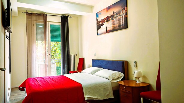 A hotel room with a bed, a nightstand, a red chair, a painting on the wall, and a window with curtains. - Charming Apartment with Garden View in enchanting Venezia (Sestiere Cannaregio)