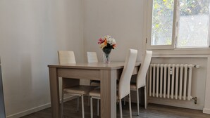 A dining area with a wooden table and chairs, a vase with flowers, and a window with a view of trees. - Charming Apartment with Garden View in enchanting Venezia (Sestiere Cannaregio)