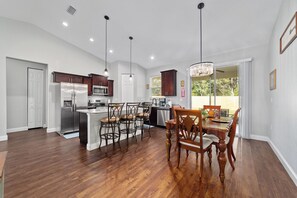 A modern kitchen with a central island, dark wooden cabinets, stainless steel appliances, and a dining area with wooden chairs and a chandelier. - Perfect Getaway #3 Near Rainbow Springs, Withlacoochee trail head and golf club (Citrus Springs)