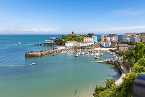 A coastal town with a marina, colorful buildings, and a historic structure on a hill. - Tenby Studio Apartment - Stroll to Beach and Town (Tenby)