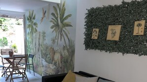 Una sala de estar con un sofá negro, cojines amarillos, una mesa de centro negra y un mural con un león y palmeras.
