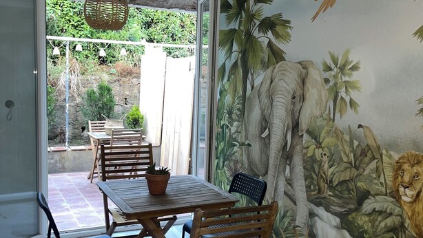 Un comedor con un mural de fauna, una mesa con sillas y una lámpara colgante.