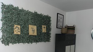 Un salón con un sofá de cuero negro, un adorno de pared con hojas verdes, un cuadro enmarcado y un armario con cestas.