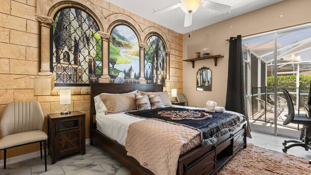 Een slaapkamer met een groot bed, een nachtkastje, een stoel, een bureau en een balkon met uitzicht.