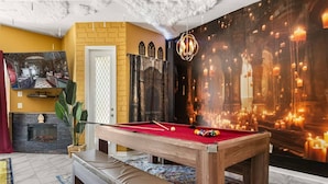Een pooltafel in een ruimte met een open haard, een groot muurschilderij en een kroonluchter.