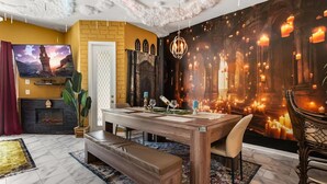 Un área de comedor con una mesa de madera, banco y sillas, una chimenea y un gran mural en la pared.