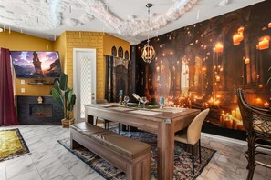 A dining area with a wooden table, bench, and chairs, a fireplace, and a large wall mural.