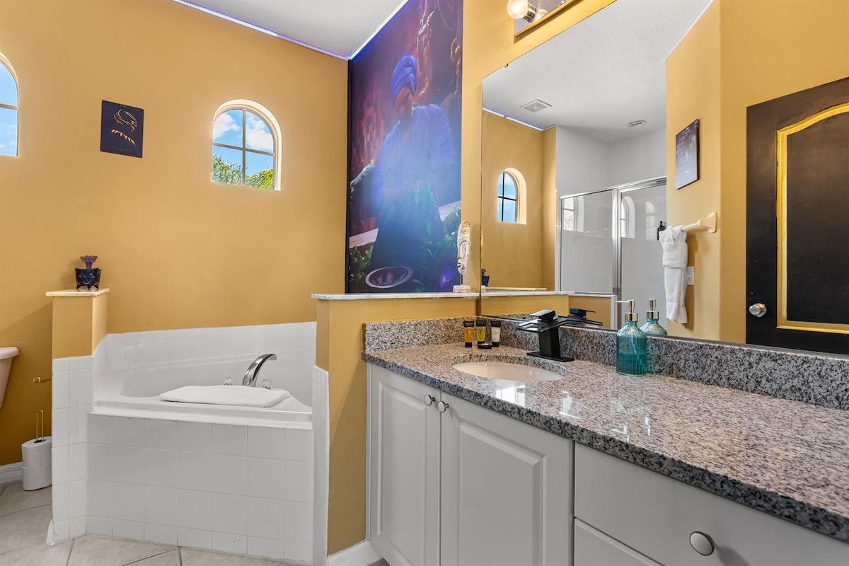 Un baño con una bañera grande, un lavamanos con encimera de granito, un espejo y una zona de ducha.