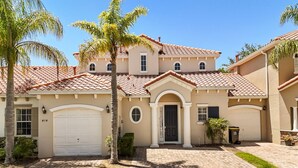 Una casa de dos pisos con fachada color beige, techo de tejas rojas y garaje delantero.
