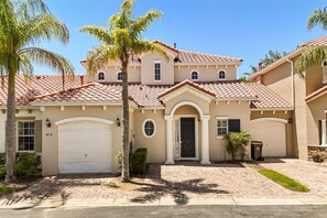 A two-story house with a beige facade, red-tiled roof, and a front garage.