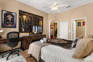 A bedroom with a bed, a desk, a chair, a ceiling fan, and a bookshelf.
