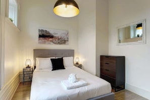Une chambre à coucher bien rangée, avec un lit, des lampes de chevet, une commode, un tableau et un miroir au mur.