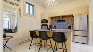 A modern kitchen with a central island, bar stools, a chandelier, and a large refrigerator.