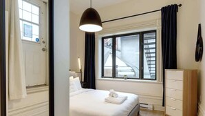 A bedroom with a bed, a dresser, a window with curtains, and a hanging light fixture.