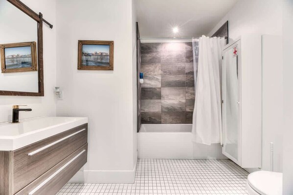 Un baño con lavamanos blanco, tocador de madera, ducha con puerta de vidrio y inodoro blanco.